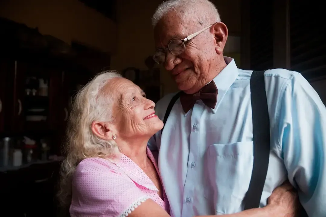 Elderly couple embracing and smiling warmly at each other indoors