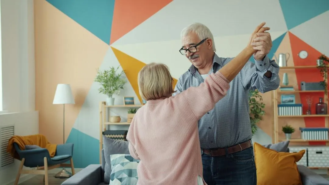 Senior couple dancing together in a bright, colorful living room, smiling and enjoying a joyful moment at home