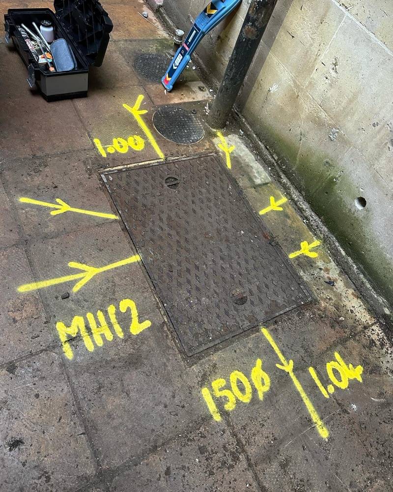 Manhole covers with detailed survey markings showing pipe diameter and invert levels