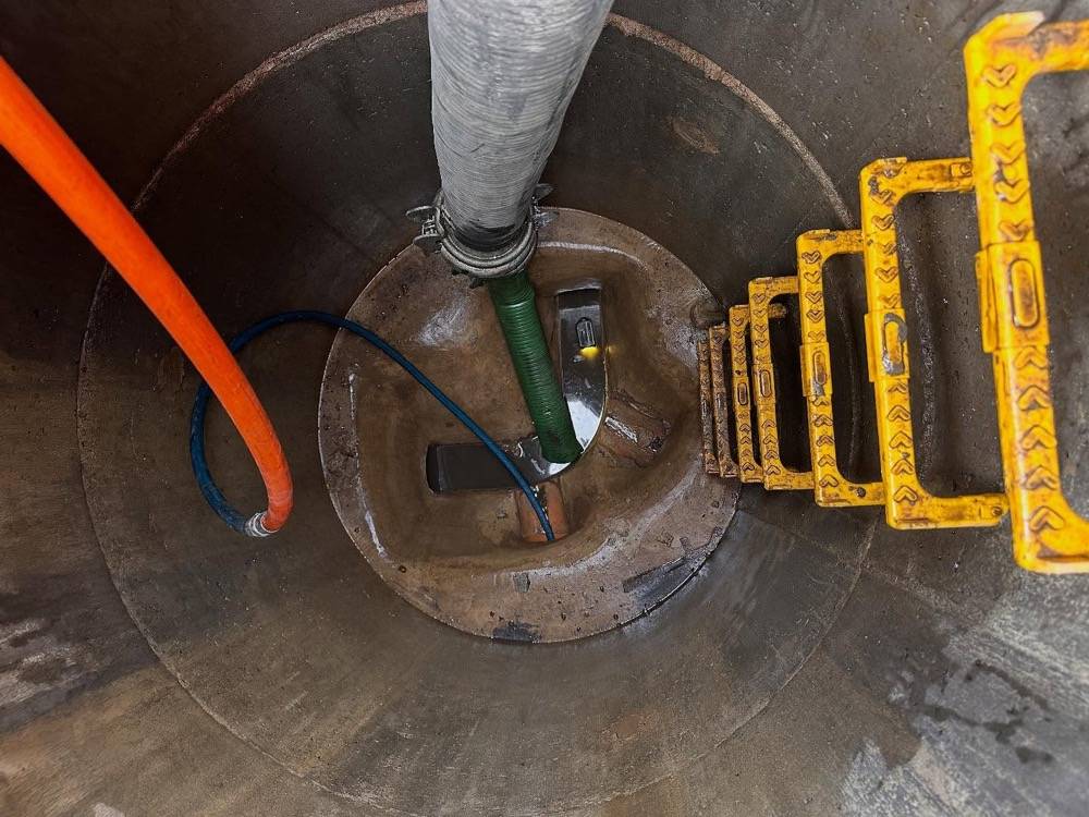 Interior of a concrete manhole chamber showing pipe connections and survey cable