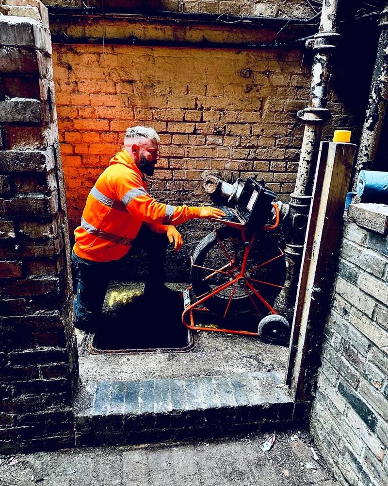 Drainage engineer operating CCTV survey equipment in an old brick cellar