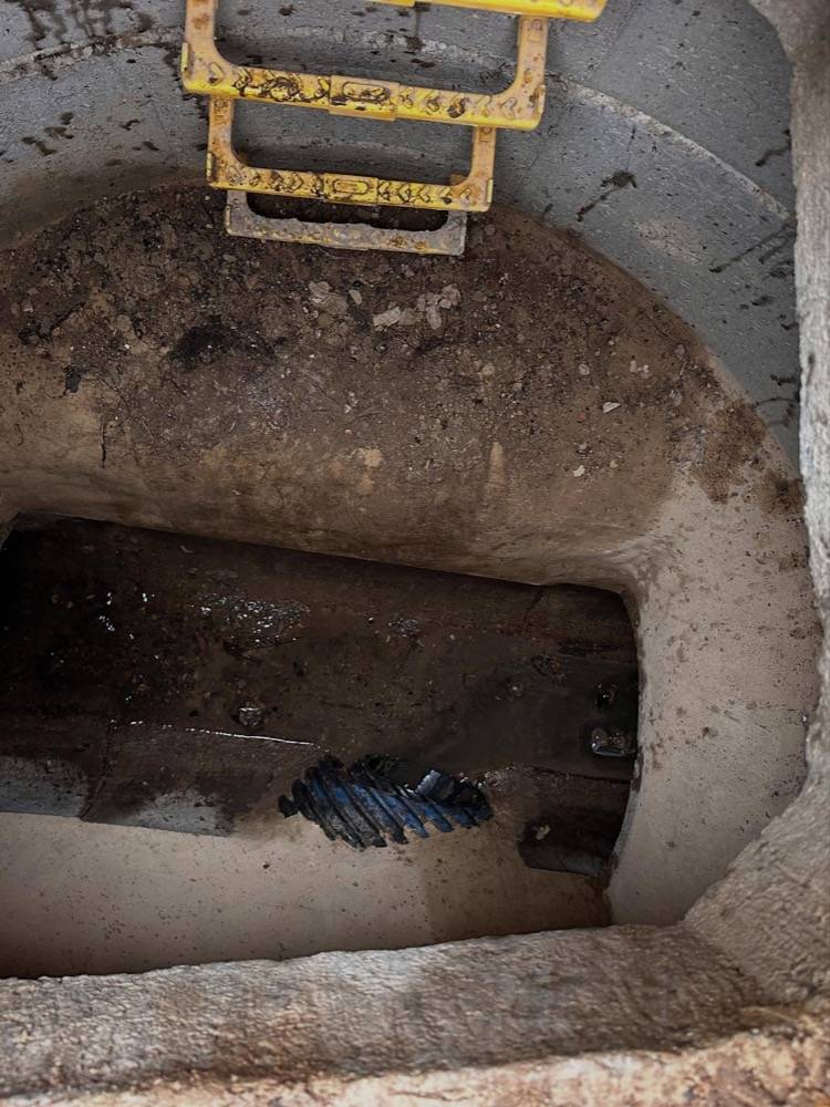 Inside a deep manhole chamber with access ladder and CCTV crawler robot at the bottom