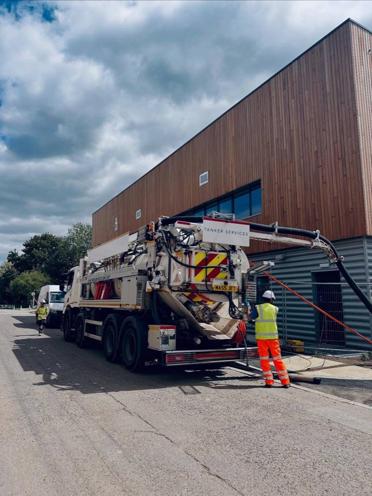 Drainage engineer operating a vacuum tanker at a modern timber-clad commercial building