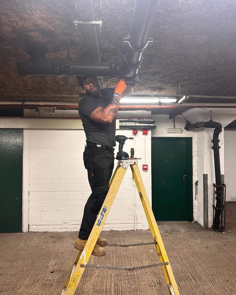 Drainage engineer on a ladder conducting maintenance work in an underground car park