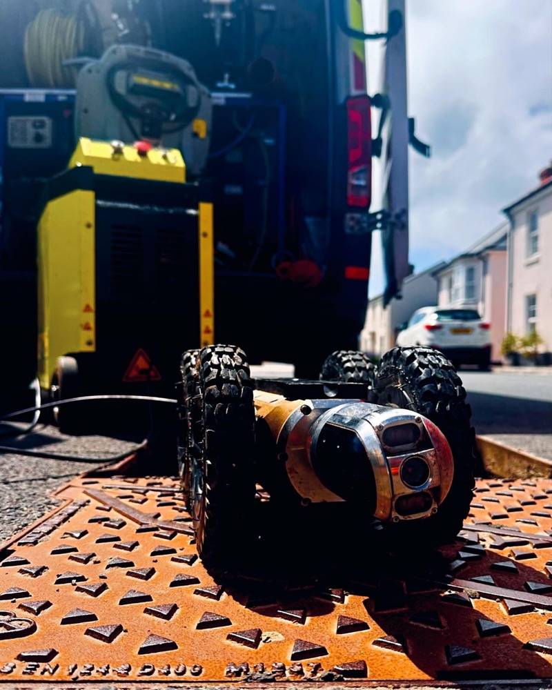 CCTV drain survey crawler robot close-up on a manhole cover with blue sky behind
