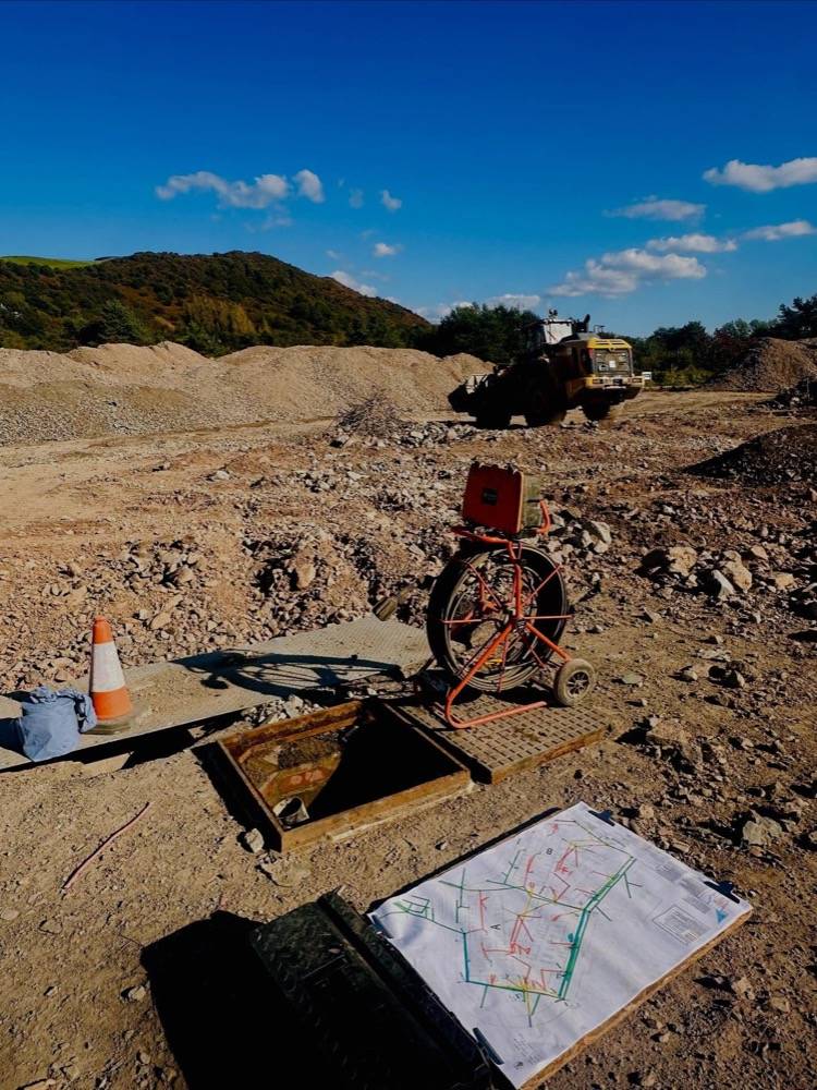 Drainage engineer with CCTV reel and drainage plan on clipboard at a quarry site