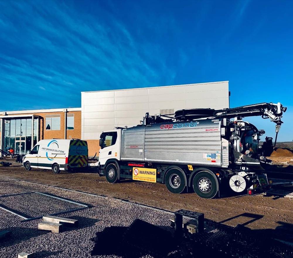 UK Drain Services vacuum tanker and van on a commercial site under blue sky