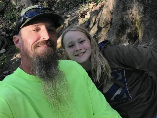 A father in a neon green shirt and cap taking a selfie with his smiling daughter outdoors.