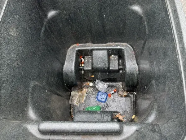 A close-up, eye-level view inside a dirty, empty black garbage can with bits of trash at the bottom.