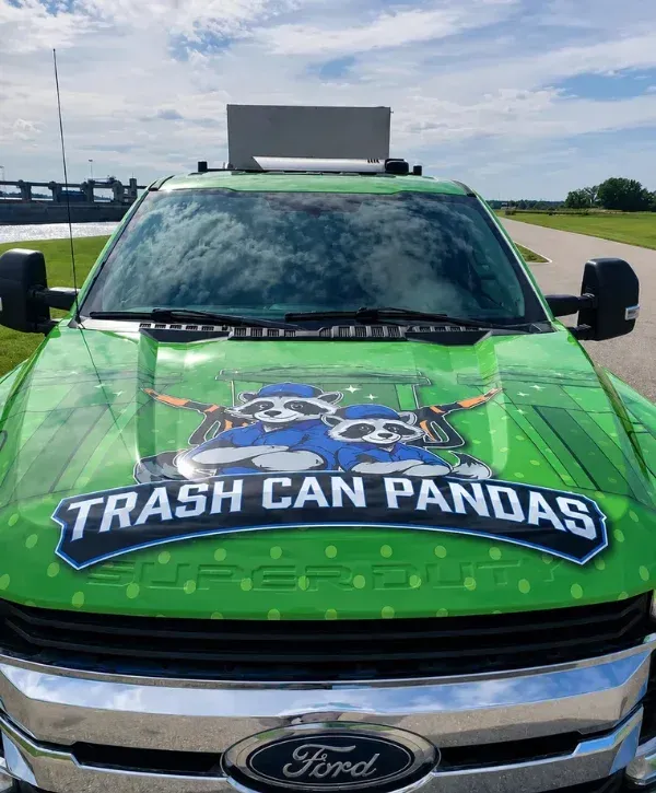 A bright green Ford Super Duty truck with a 'Trash Can Pandas' logo featuring two raccoons on the hood.