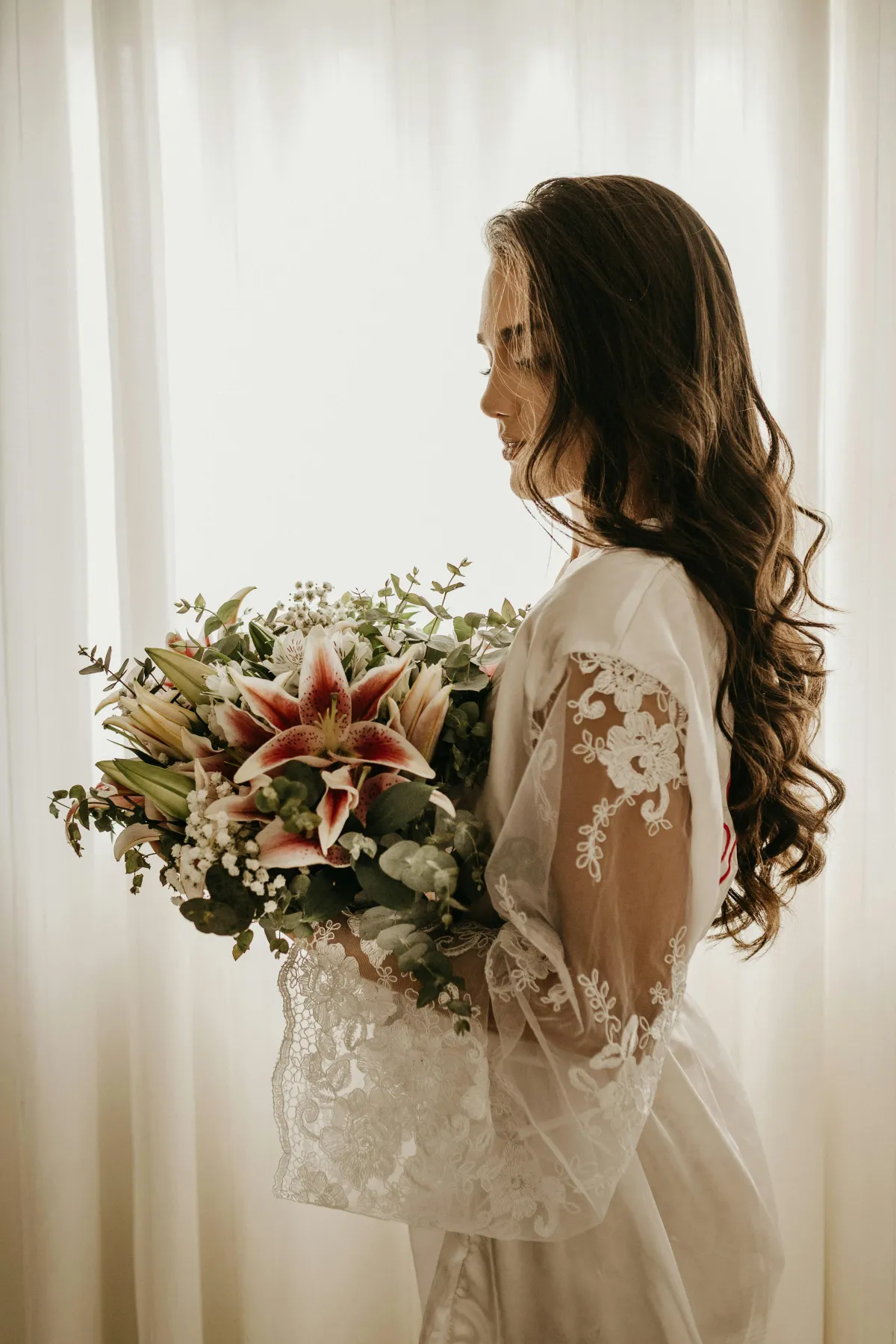 Bride in a robe with finished hair and makeup holding her bouquet before photos