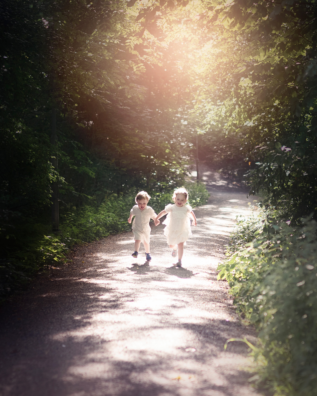 Två små barn springer hand i hand längs en skogsväg under Outdoor Mini Moments.