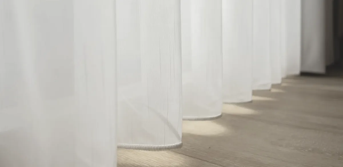 Bespoke technical sheer drapery featuring continuous lead-weighted hem for zero-deviation verticality in architectural projects.