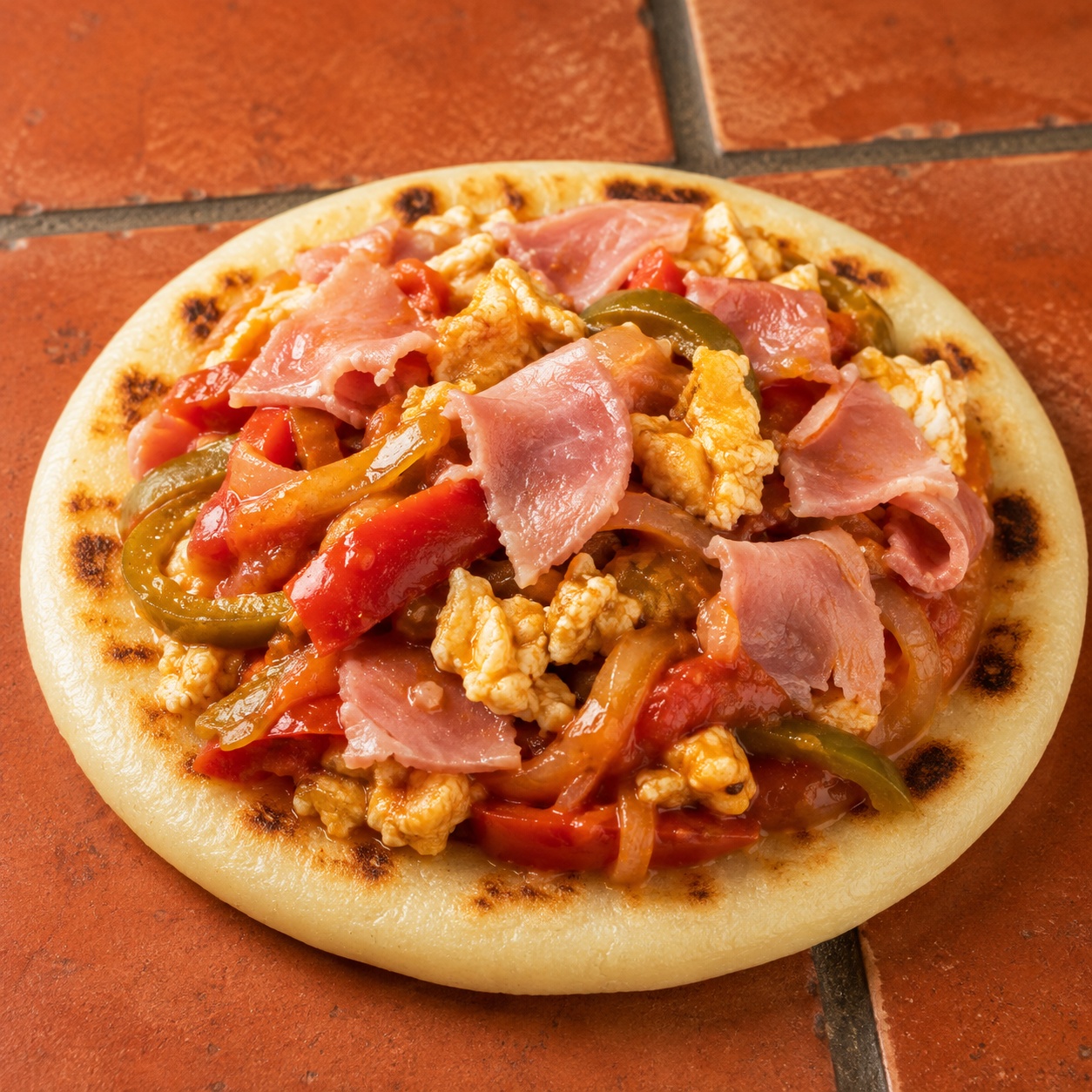 Arepa topped with Basque piperade, scrambled egg and torn ham