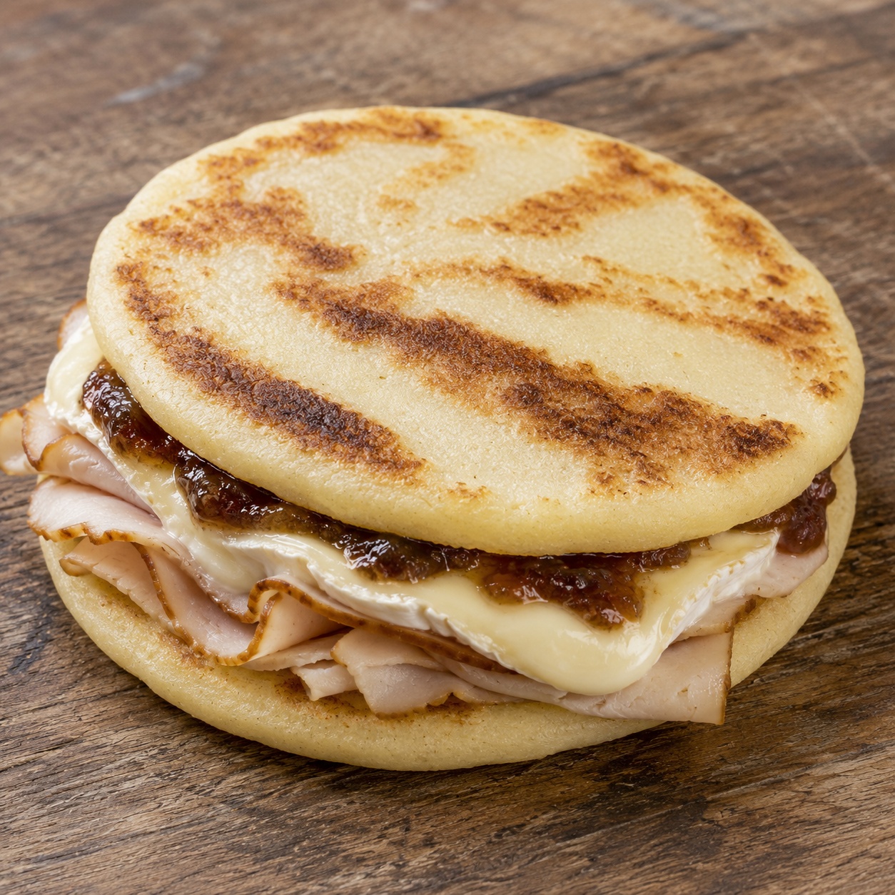 Two arepas pressed together with smoked turkey, melted brie and apple butter