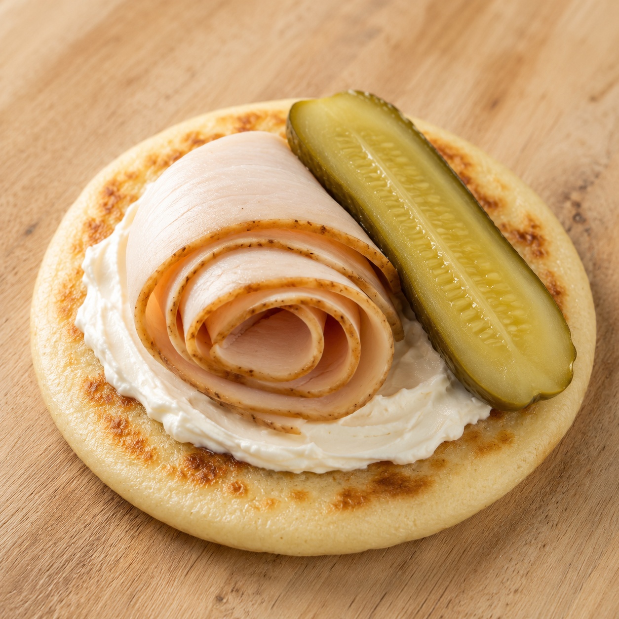 Arepa with cream cheese, a rolled turkey slice and pickle spears