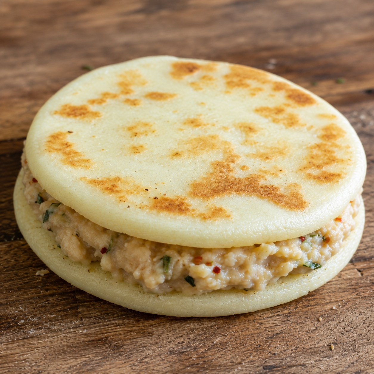 Two arepas sandwiched with creamy smashed white beans flecked with rosemary and chili