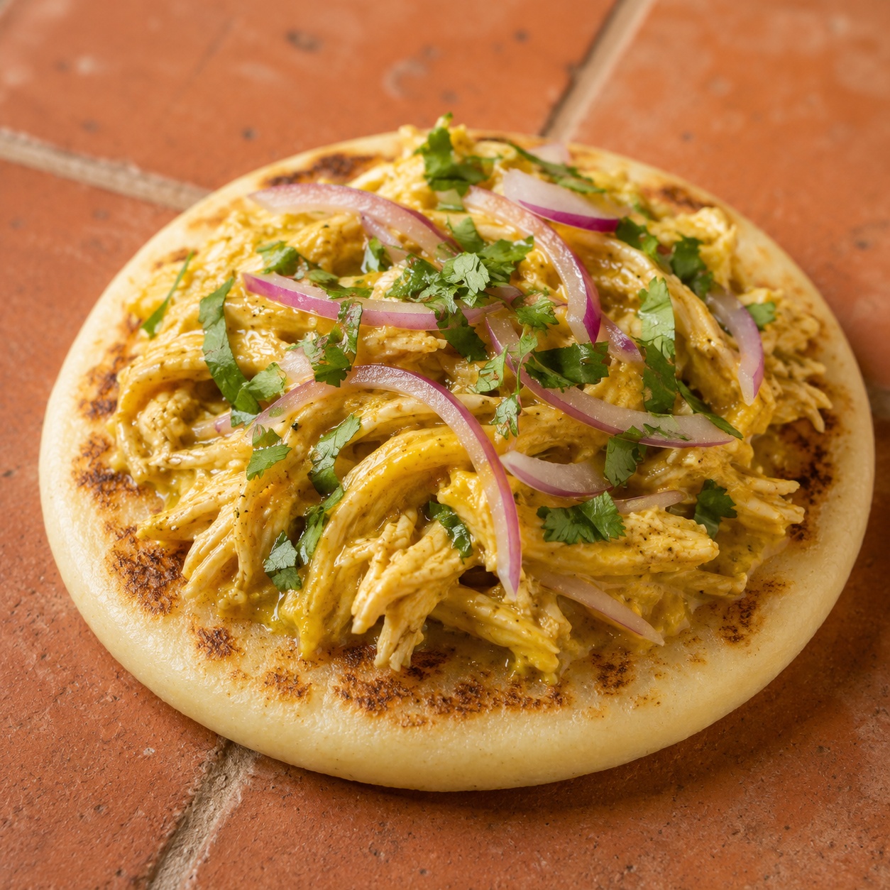 Arepa topped with shredded chicken in golden aji amarillo sauce with red onion