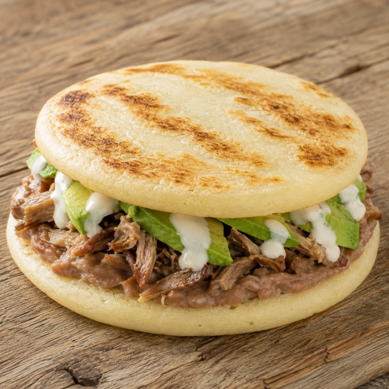 Two arepas pressed together with refried beans, carnitas and avocado