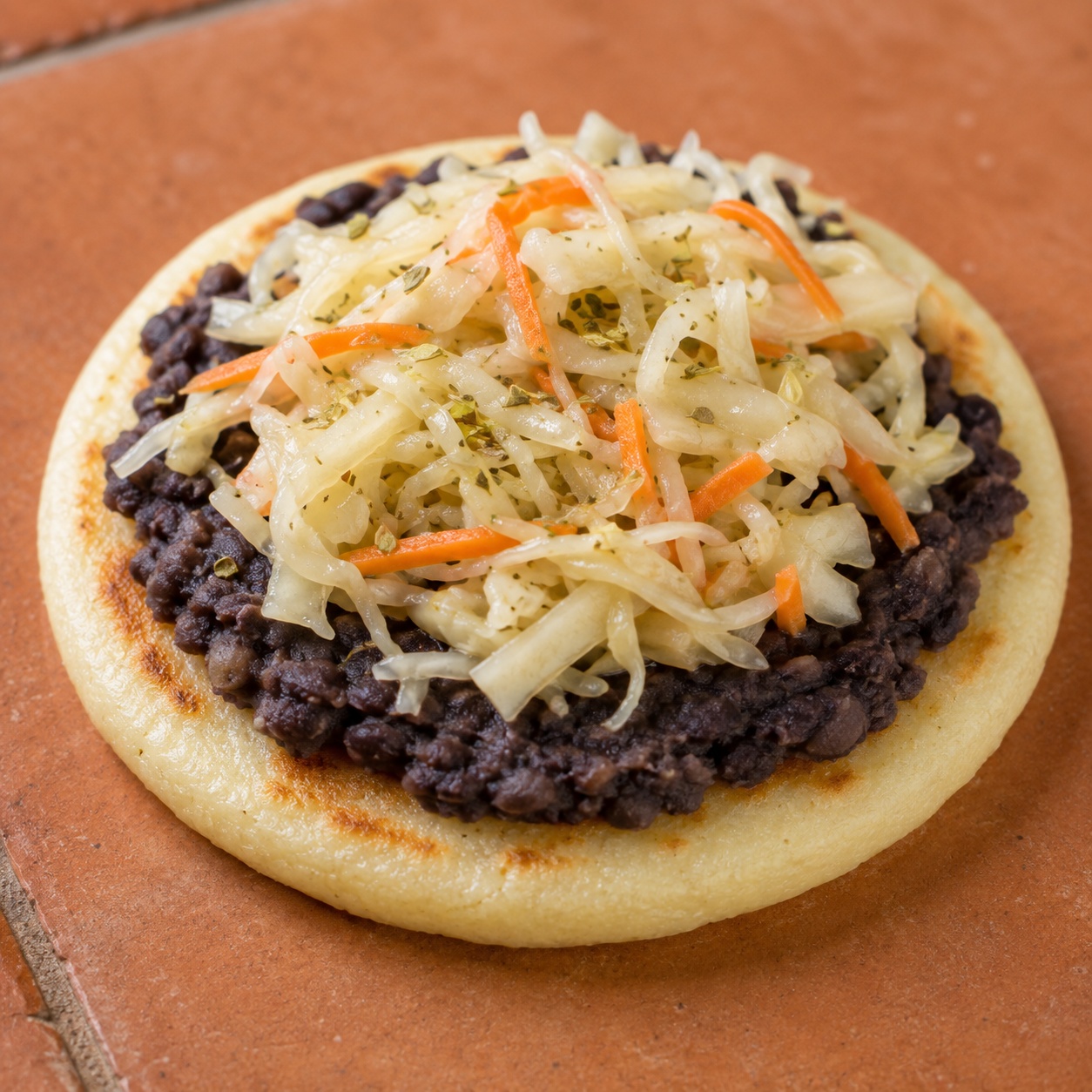 Arepa topped with mashed black beans and tangy cabbage curtido