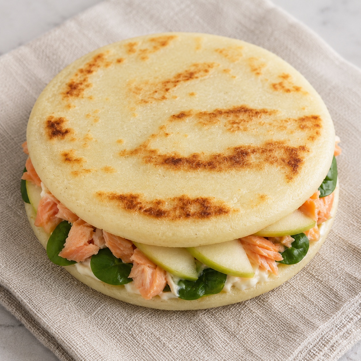 Two arepas sandwiched with flaked smoked trout, apple slices and horseradish cream