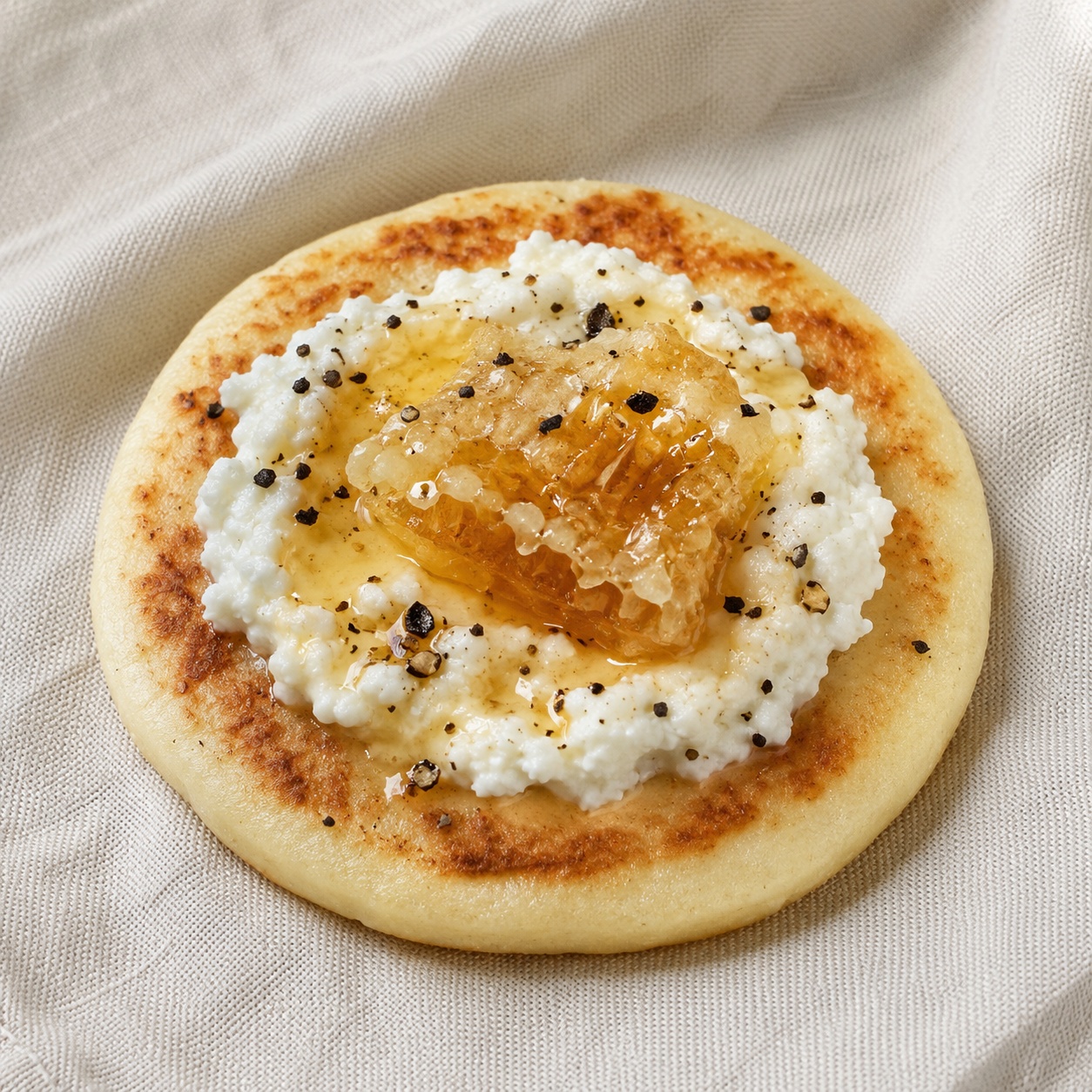 Arepa spread with goat cheese, a piece of honeycomb and cracked black pepper