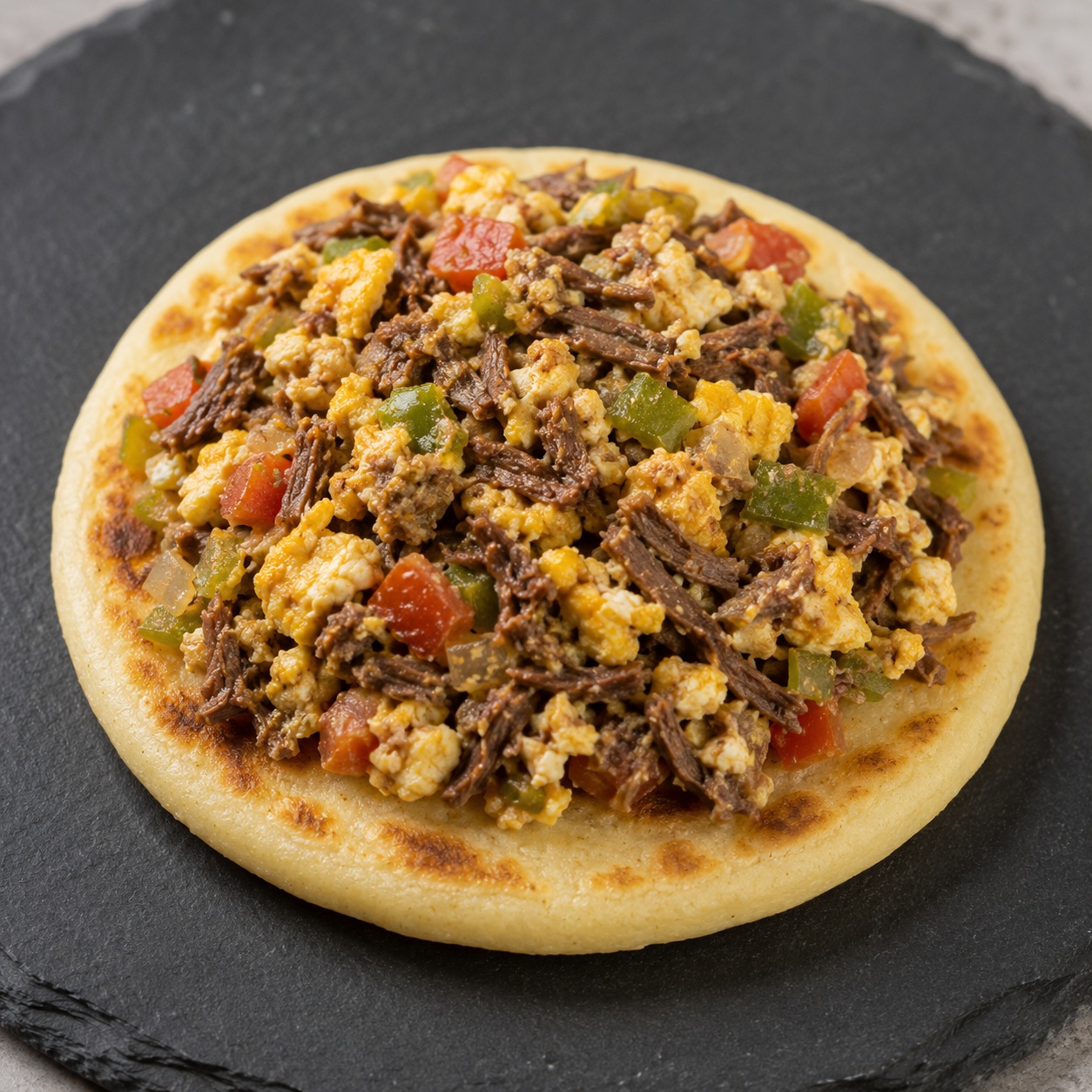 Arepa topped with shredded beef scrambled with eggs, onion and pepper