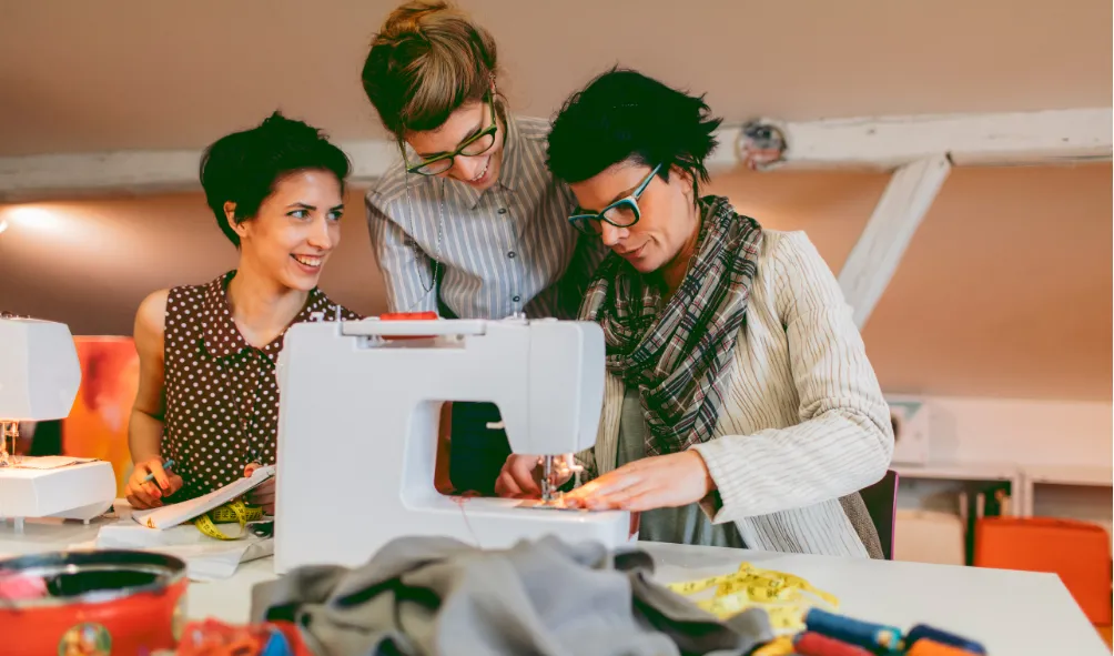 A group of women around a sewing machine, working on their sewing projects.