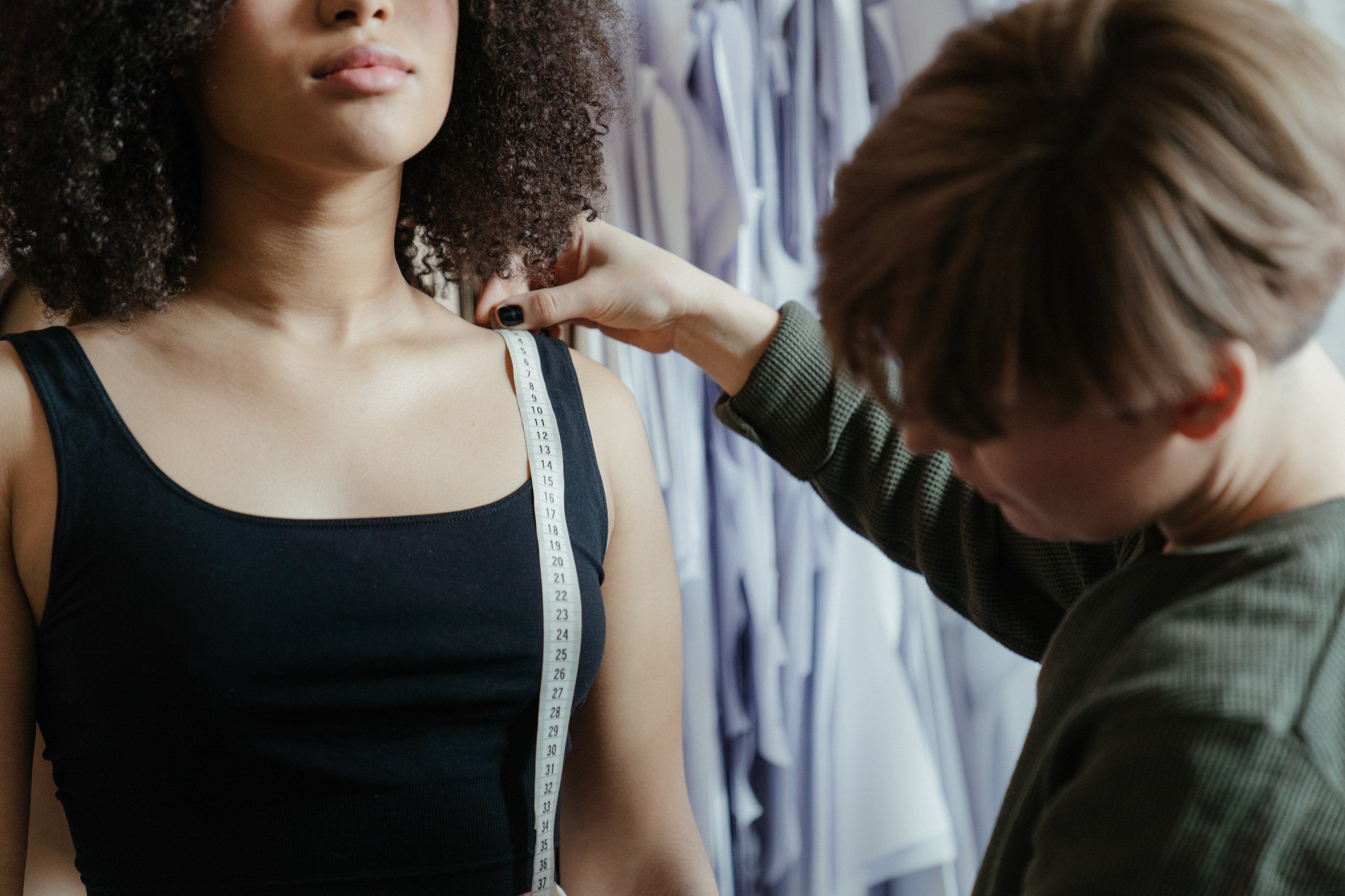 A dressmaker measuring a woman with paper patterns in the background. 