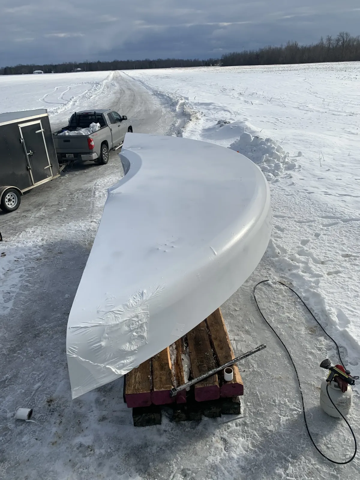 Large shrink wrapped component sitting on timber cribbing in deep snow with a truck and trailer behind