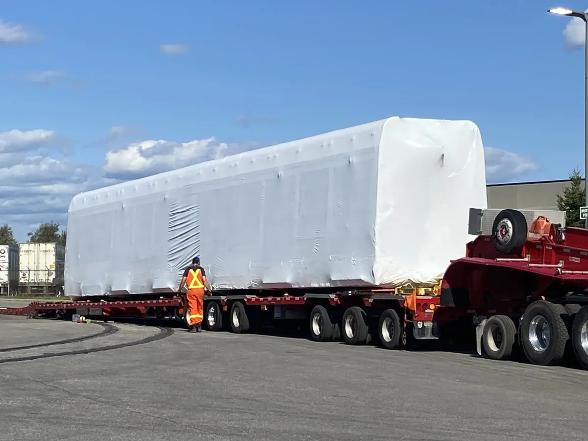 Very large shrink wrapped load on a multi-axle heavy haul trailer with a worker in high visibility clothing alongside