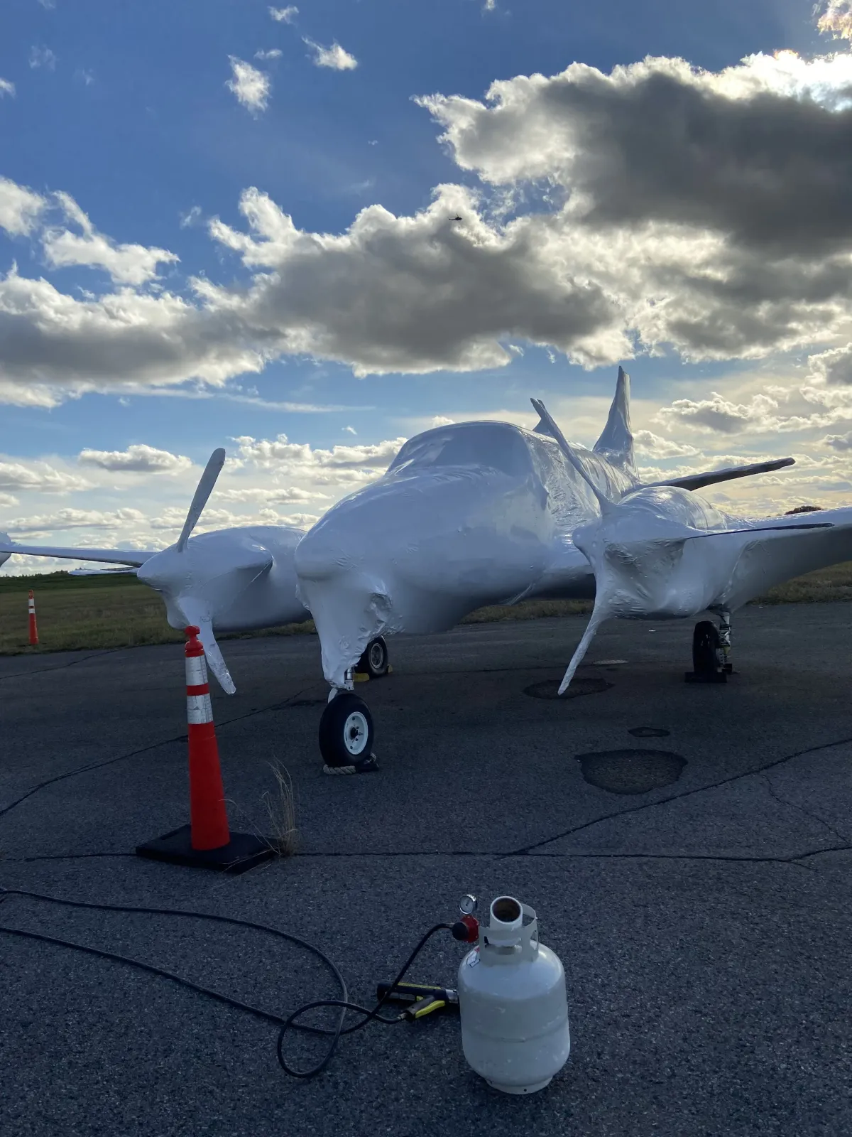 Light aircraft fully shrink wrapped in white film on an airfield apron, propane heating equipment in the foreground