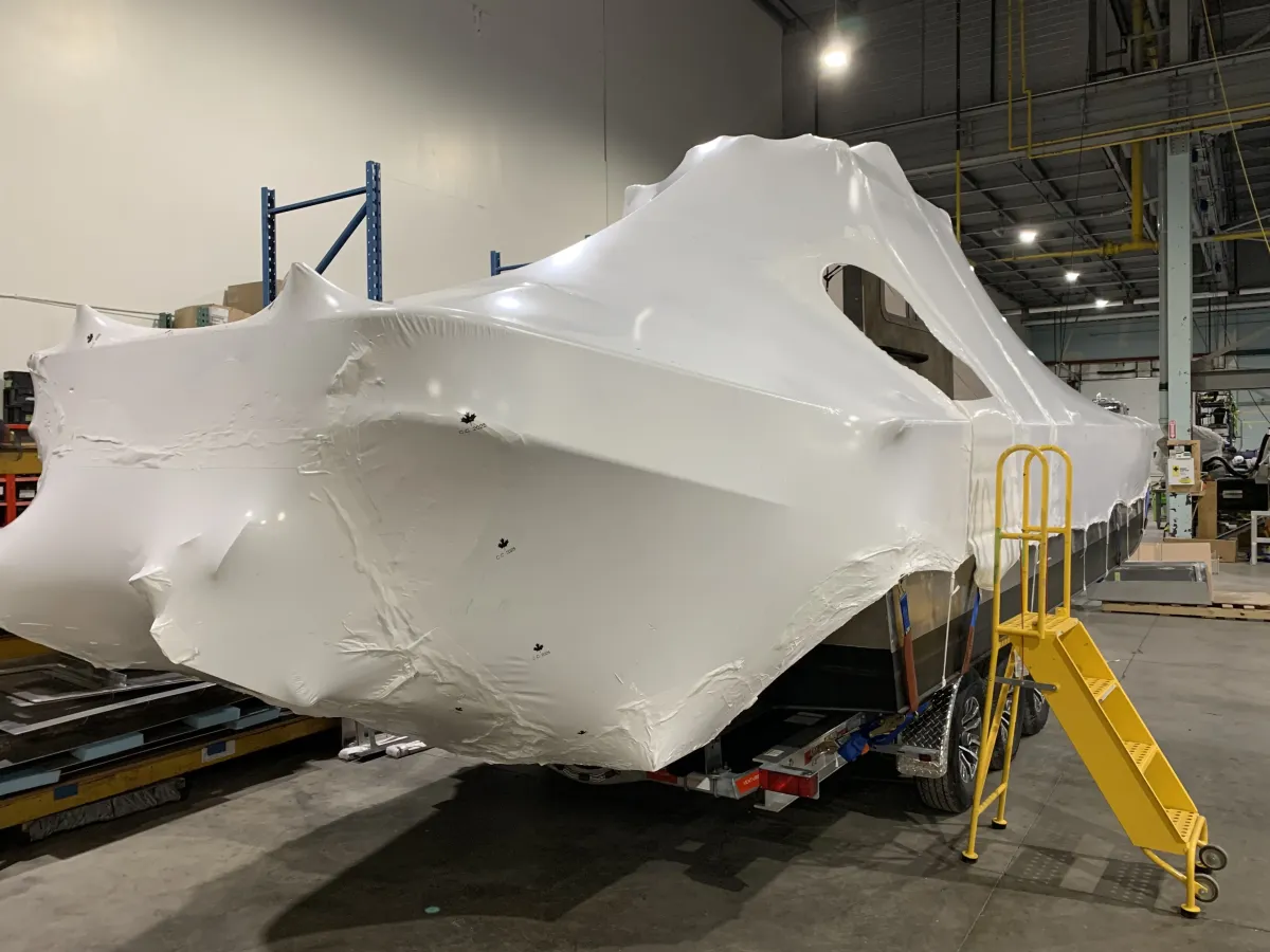 Large industrial unit fully sealed in taut white shrink film inside a plant, with access stairs alongside