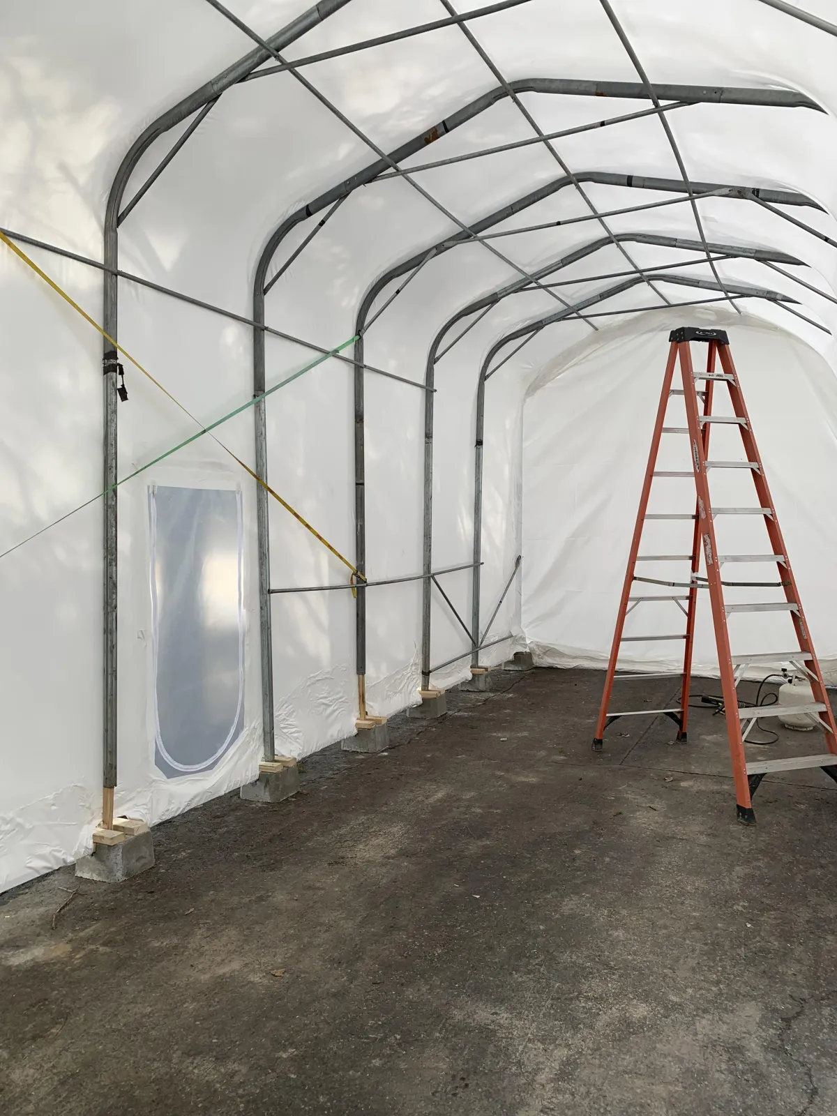 Inside a shrink wrapped temporary enclosure showing the steel support frame, tensioned white film and a zippered access door