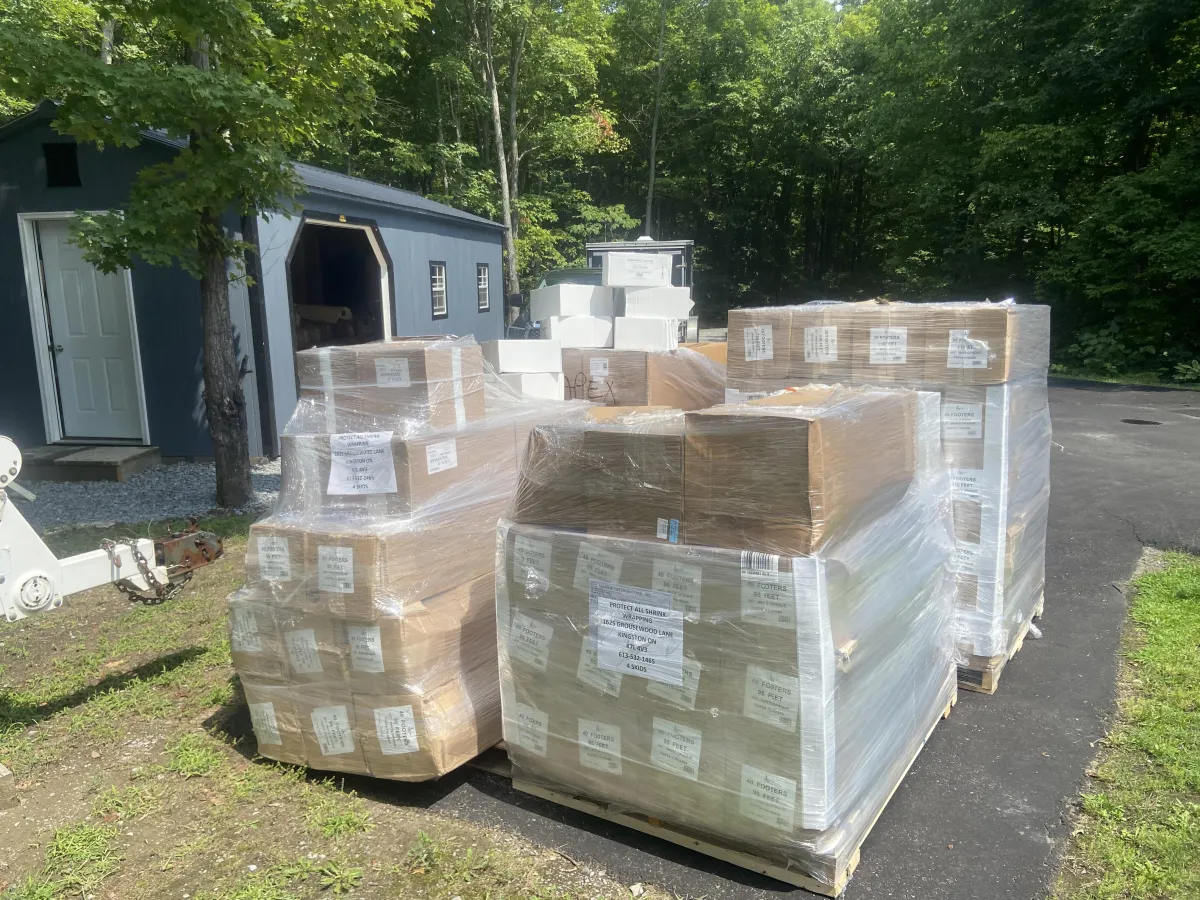 Stacked pallets of boxed goods wrapped in protective film outside a building