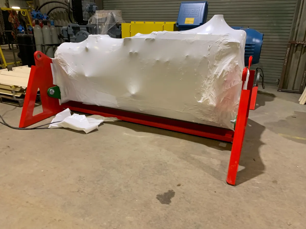 Industrial machinery shrink wrapped in white film inside a workshop, with compressed gas cylinders stored in the background