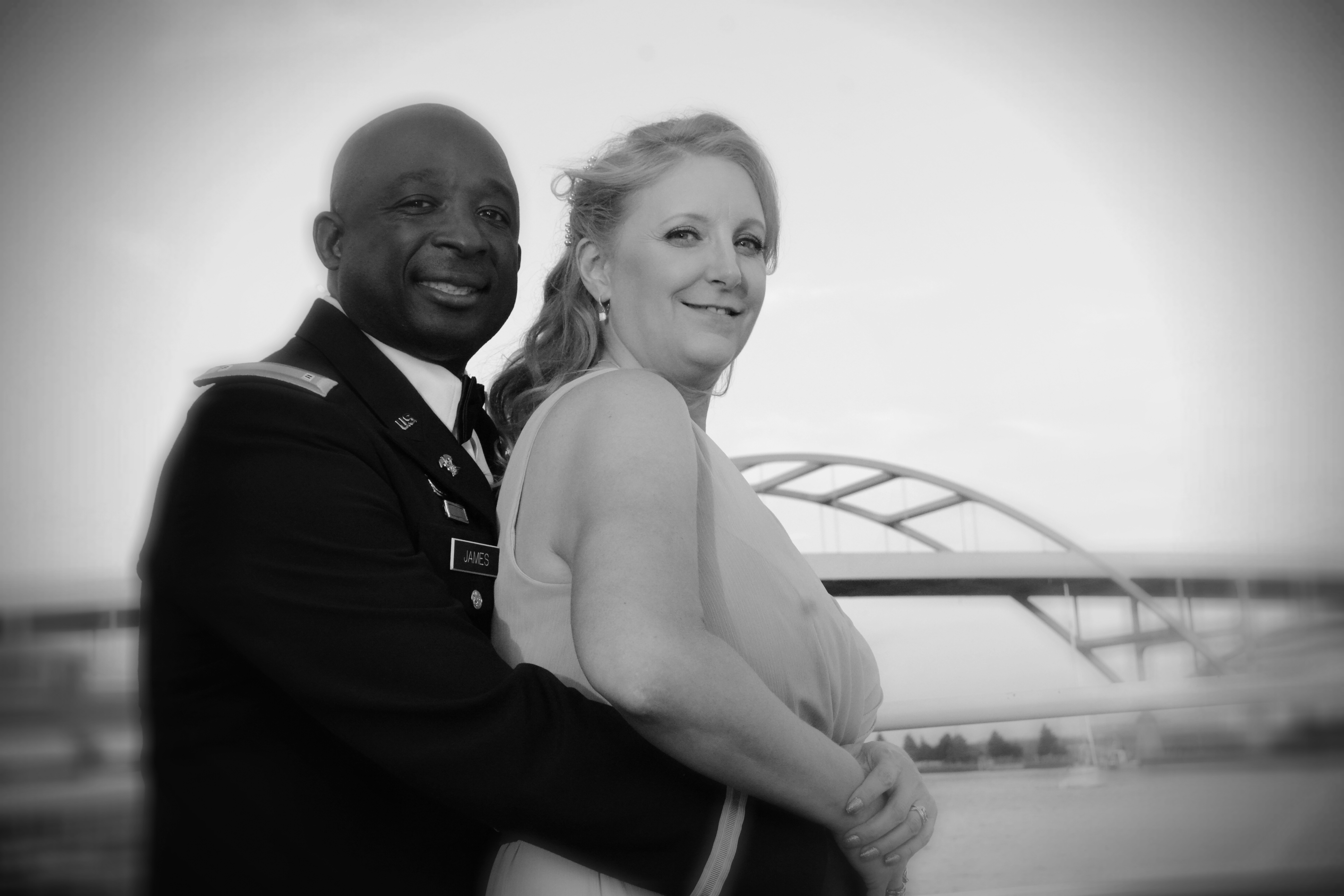 A joyful bride and groom embrace in a golden field at sunset, the bride’s veil flowing in the breeze, both smiling radiantly. The background is softly blurred, highlighting the couple’s happiness and the warm, romantic atmosphere.