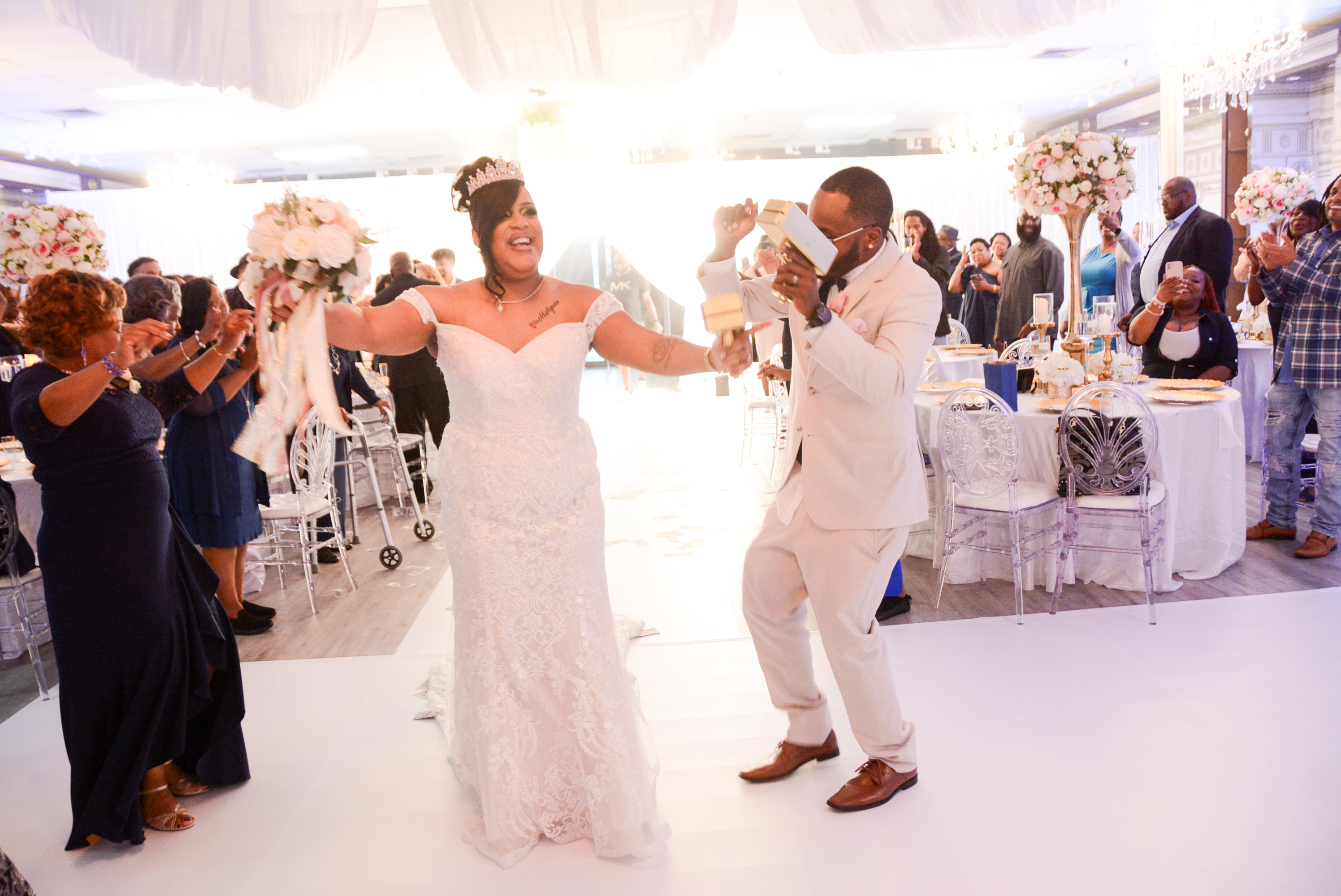 A wide shot of an outdoor wedding ceremony in a lush garden, guests seated in white chairs, floral arch in the background, and sunlight filtering through trees, creating a dreamy, romantic setting.
