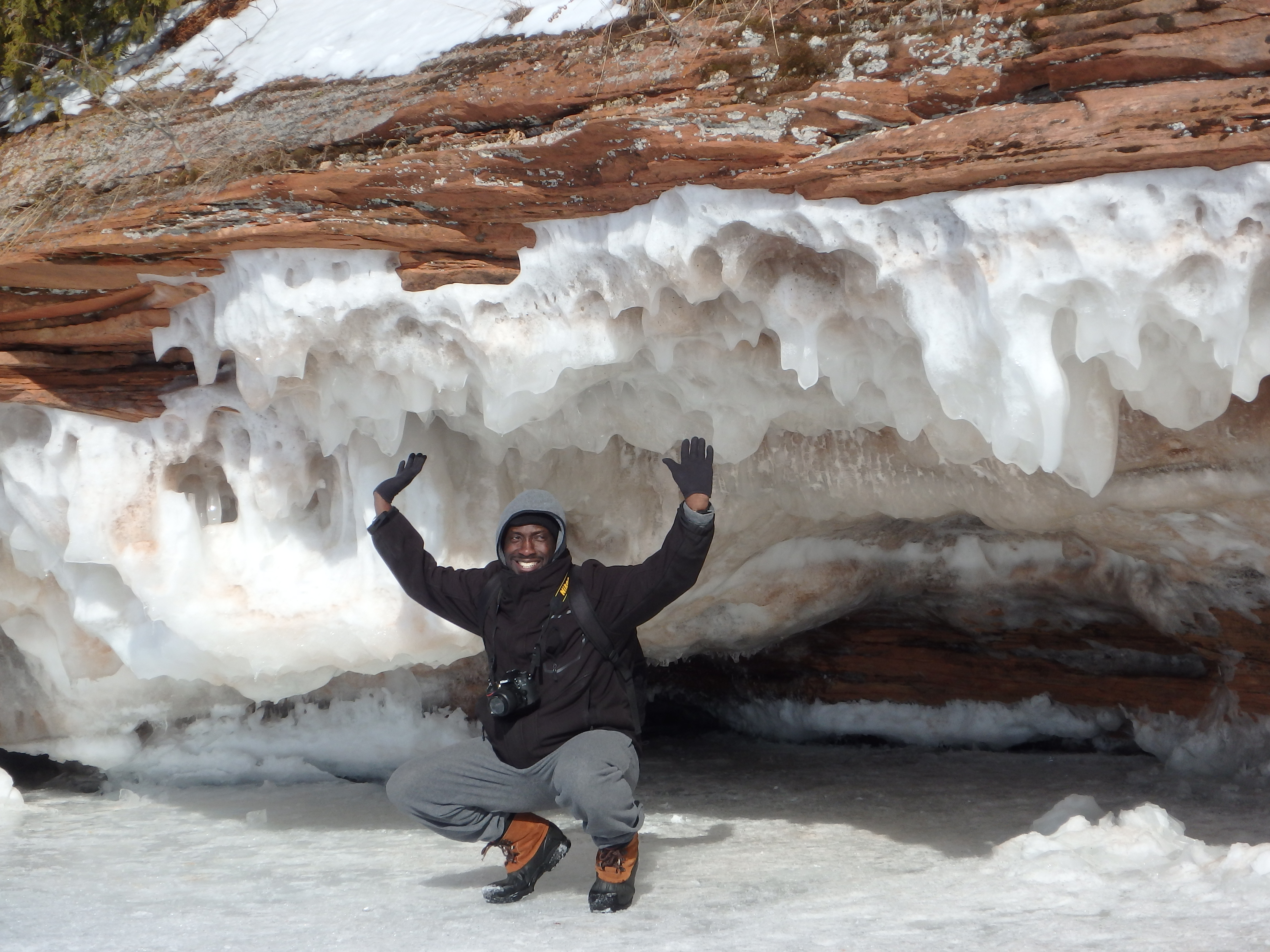 A professional photographer, mid-30s, with short dark hair and glasses, holding a DSLR camera in a bright studio. The background features soft lighting, shelves with photo books, and a large window, creating a creative and welcoming workspace.
