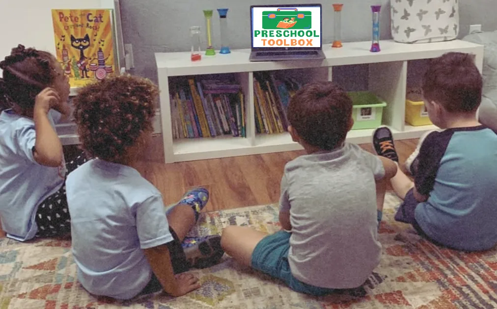 Students sit in a semicircle watching the teacher on a laptop