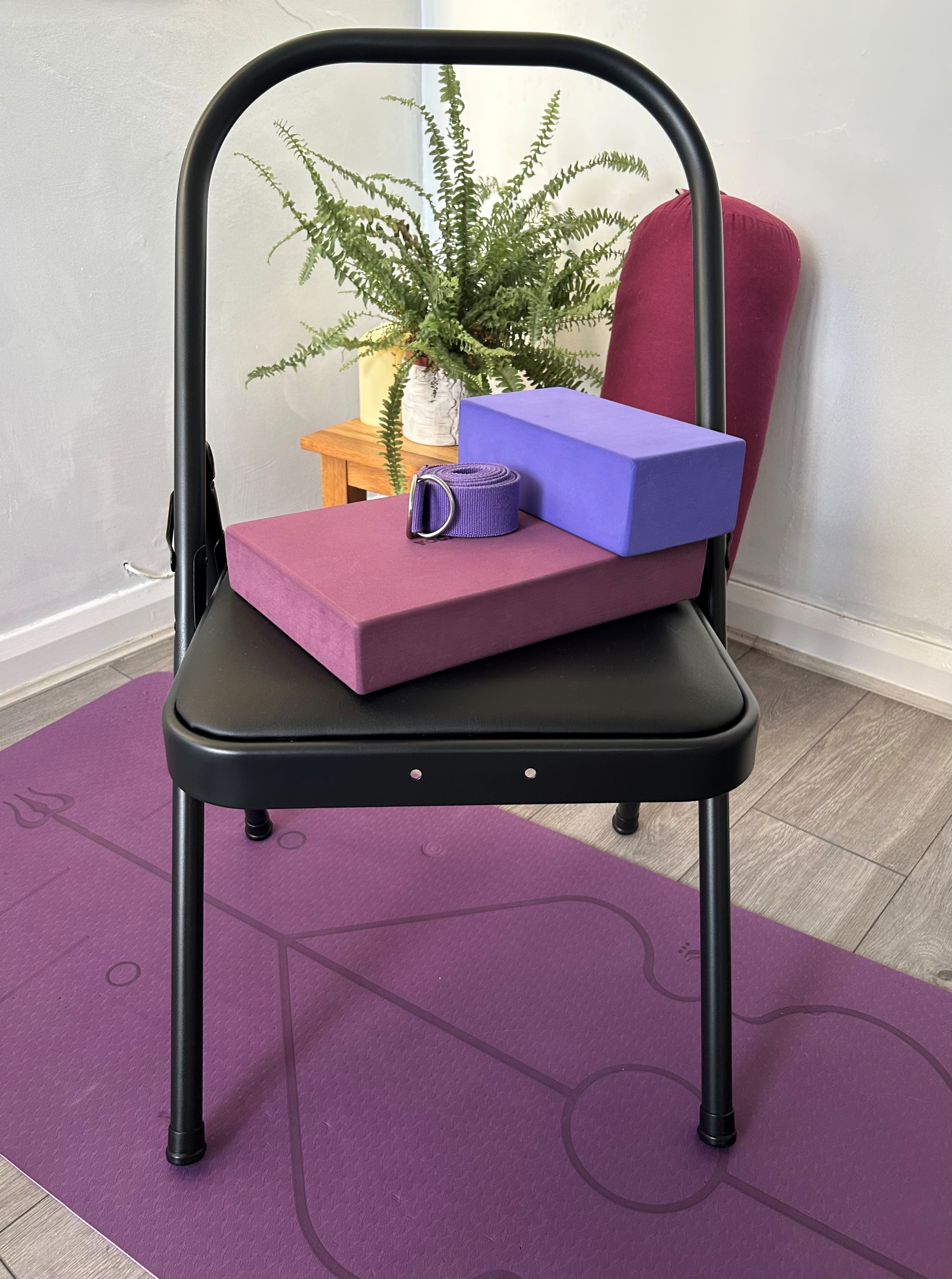 Yoga chair on a mat with yoga block, strap and bolster, used for gentle and accessible yoga movement.