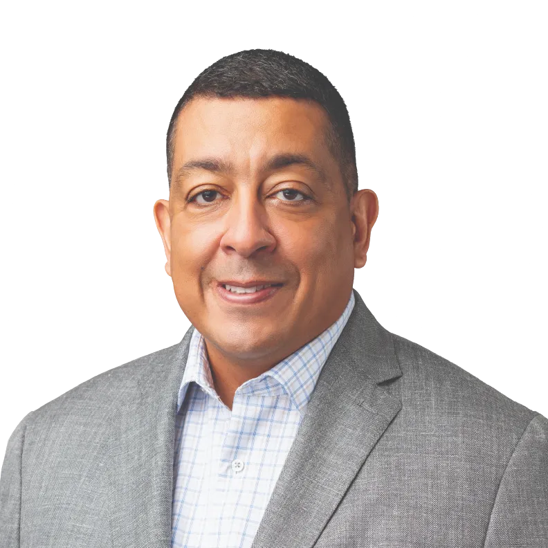 A confident, mid-30s female instructor of South Asian descent stands in front of a digital whiteboard displaying complex code and security diagrams. She gestures toward the board, engaging a small, attentive group of students. The setting is a high-tech classroom with blue accent lighting.