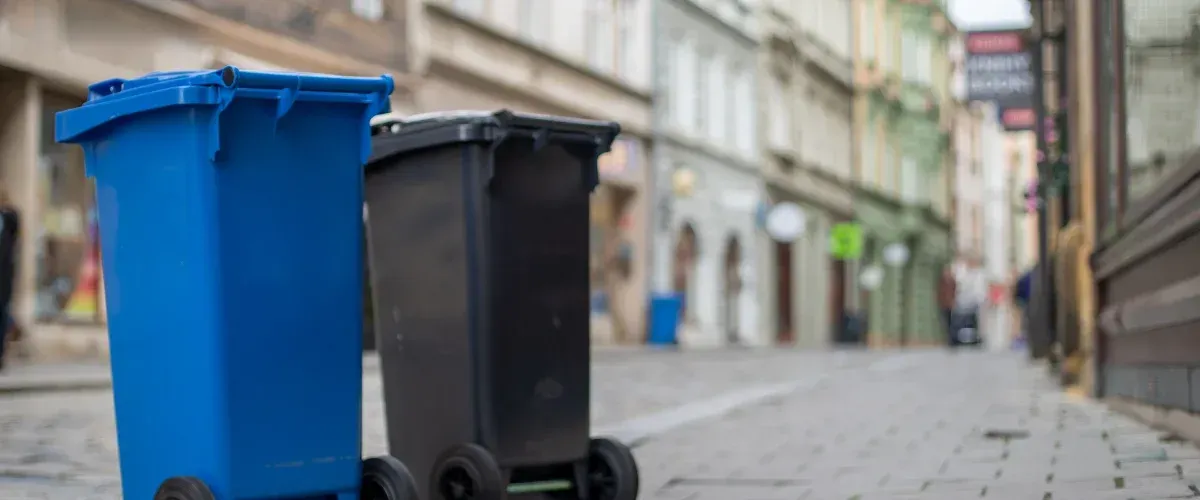 A shallow depth of field shot of a bright blue and black waste bin on a cobblestone street.
