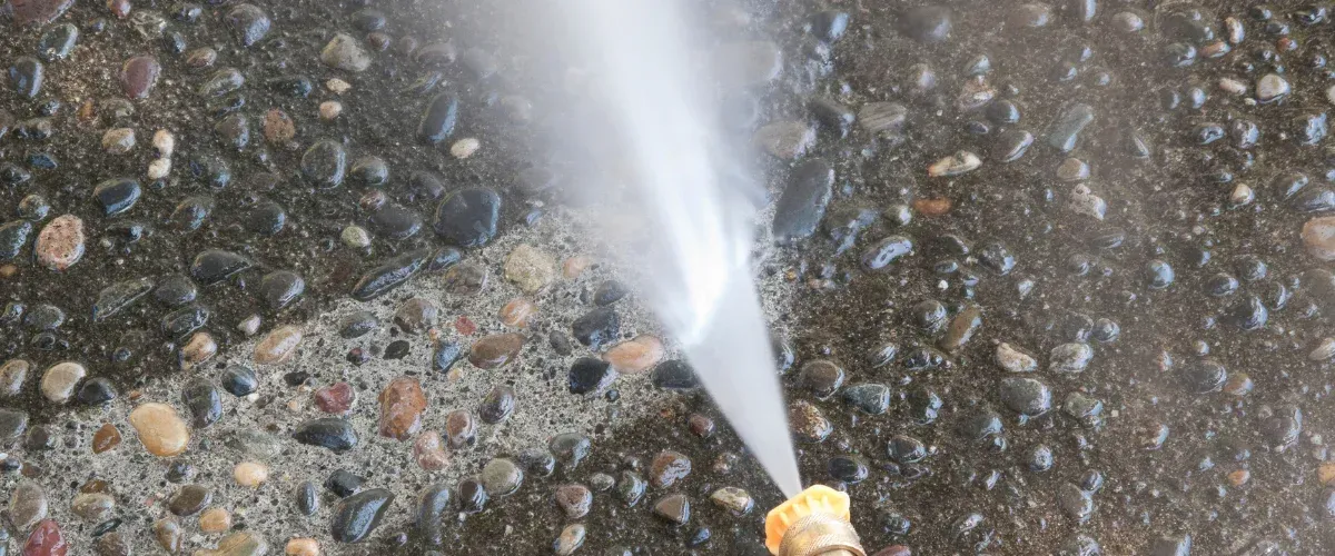 A close-up view of a person using a high-pressure washer to clean a tiled patio and steps, removing dirt.