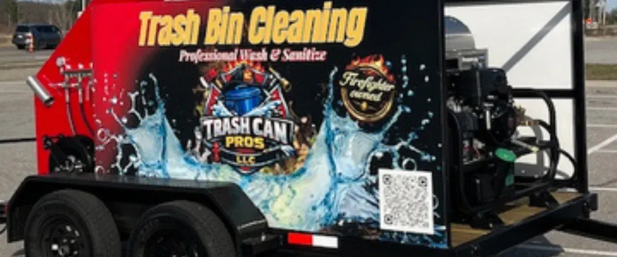 Side view of a red and black trailer for 'Trash Bin Cleaning' with 'Professional Wash & Sanitize' text, a 'Trash Can Pros LLC' logo, and 'Firefighter owned' seal.