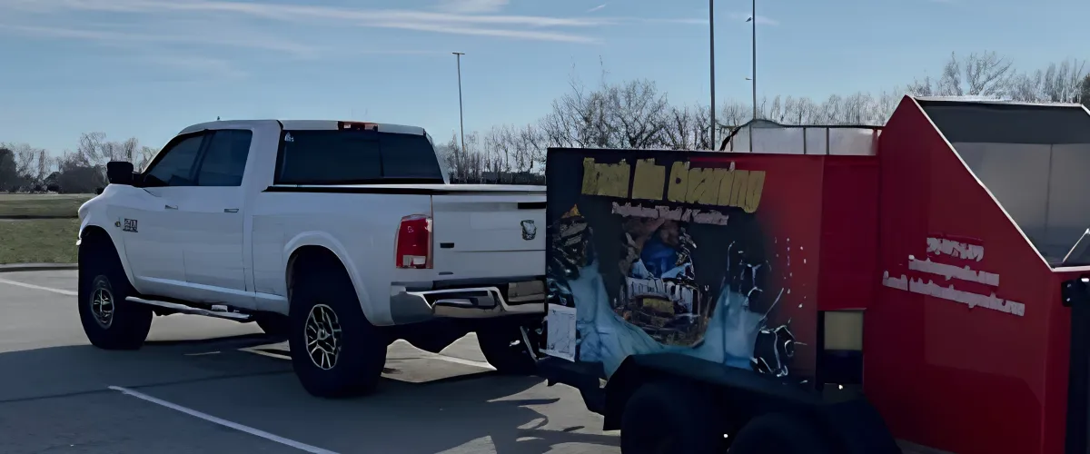 A white pickup truck with tinted windows towing a red and black trailer with graphics, parked outdoors on a clear day.
