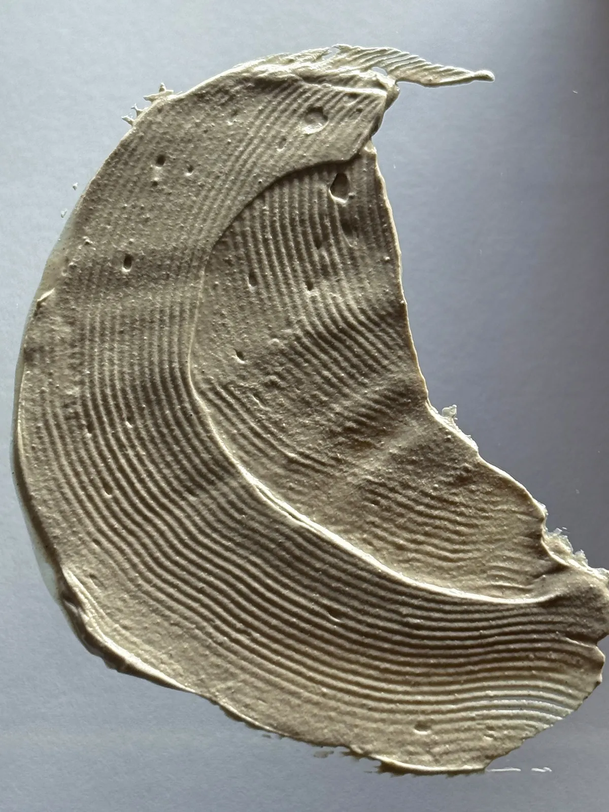 Close-up of the I AM Weekly Rejuvenating Mask gray-beige clay texture in a curved swipe