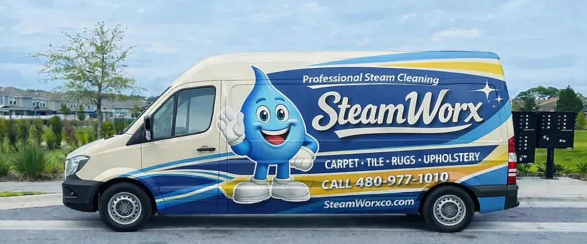 A white SteamWorx van with blue and yellow accents, and a cartoon water-drop mascot on the side, parked on an asphalt road.