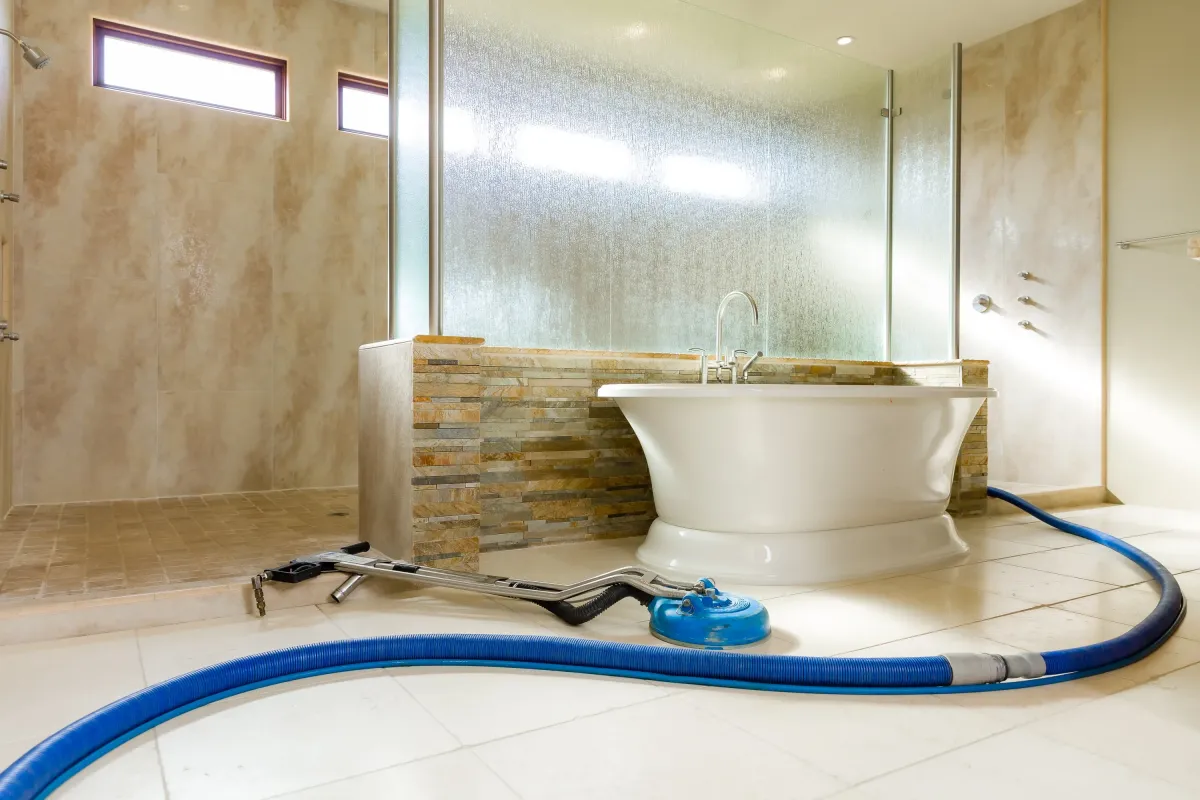 Professional tile and grout cleaning equipment in a modern residential bathroom with blue extraction hose and floor cleaning tool.