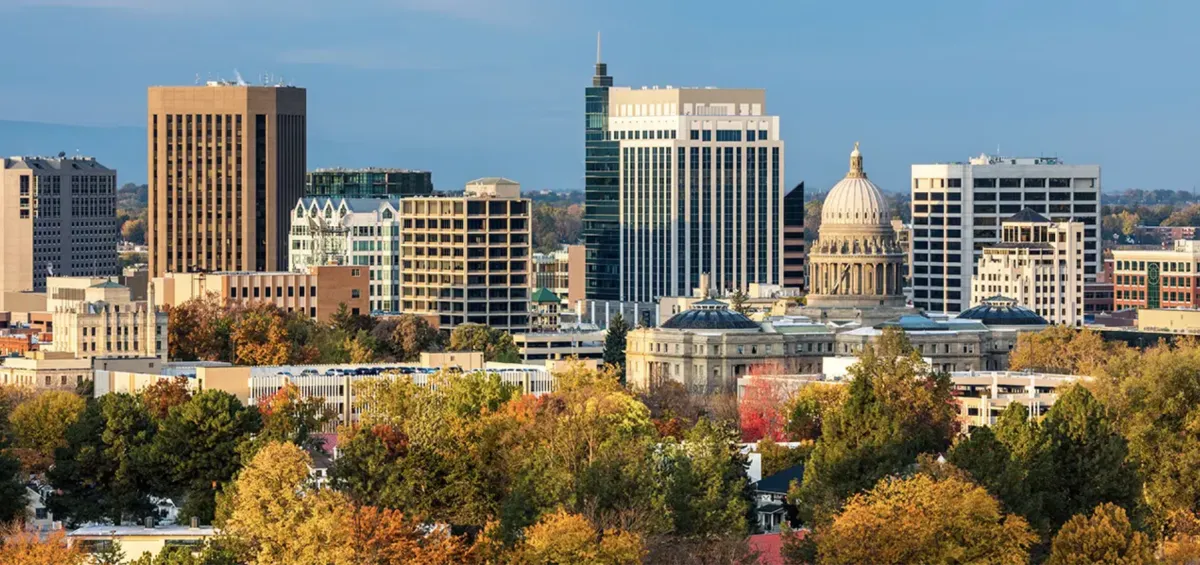 A friendly recruiter sitting at a desk with a laptop and headset, ready to answer questions, with a bright orange accent wall and plants in the background. The recruiter is smiling and approachable.